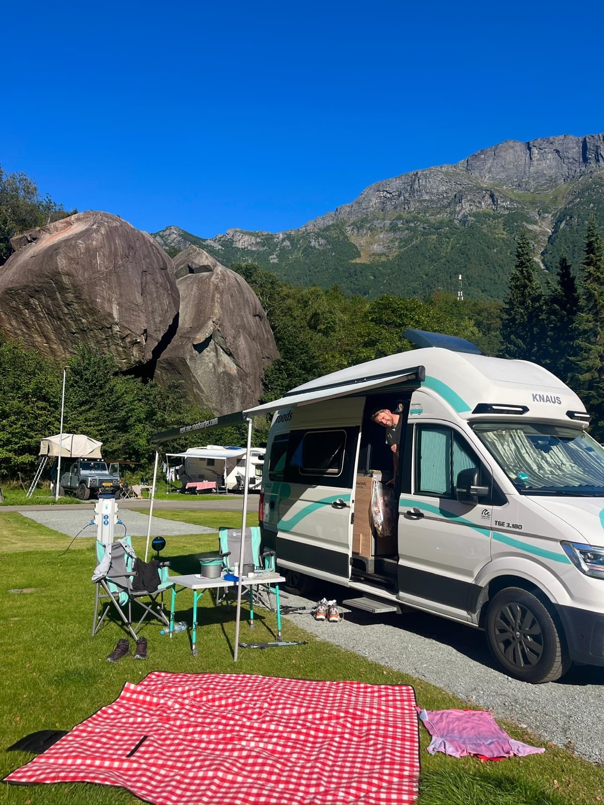Jonas schaut aus der Schiebetür des Campers, dahinter große Felsblöcke und steile Berge