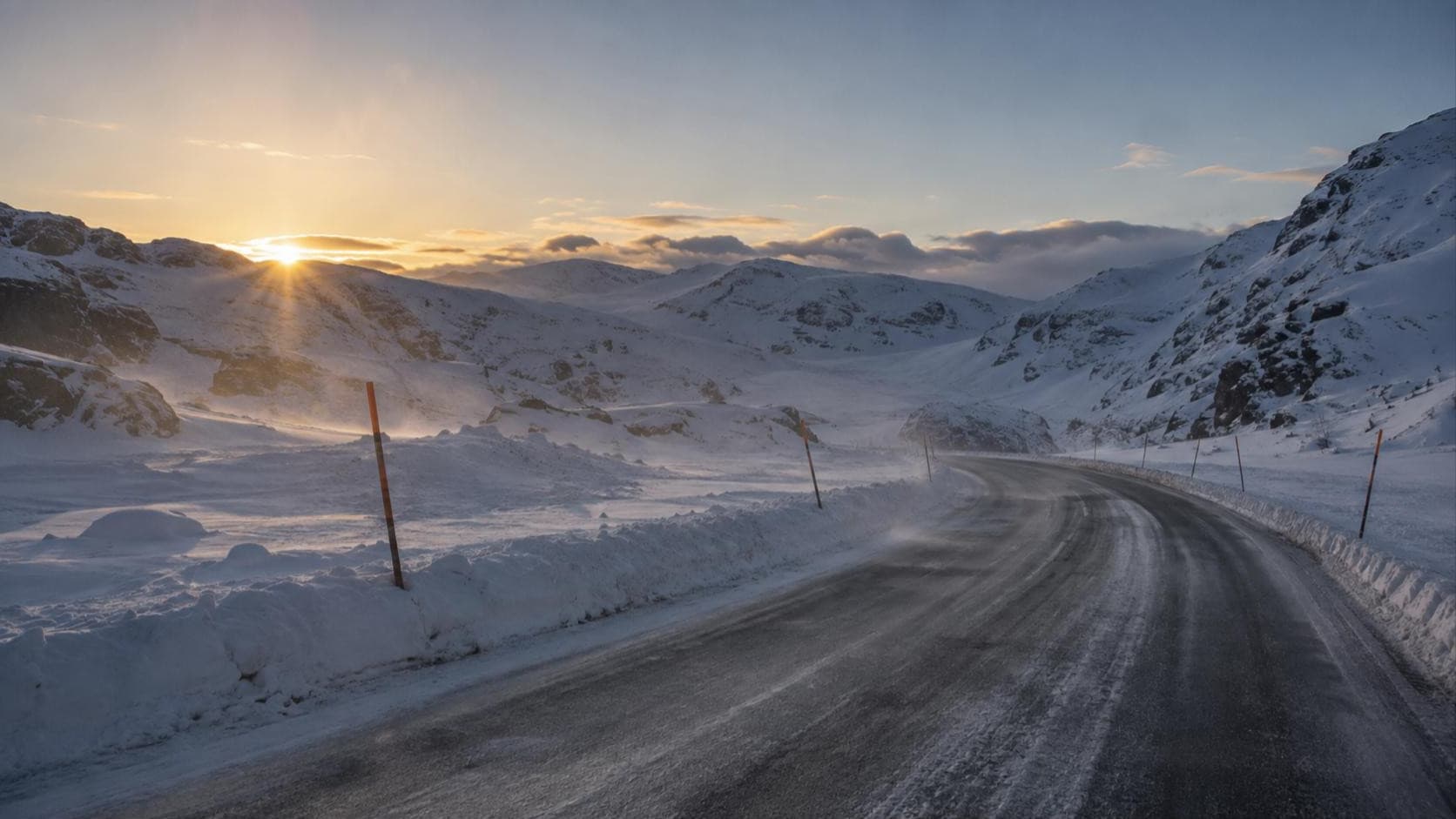Leere Passstraße im Winter bei Sonnenaufgang, gesäumt von Schneestangen und Schneewällen