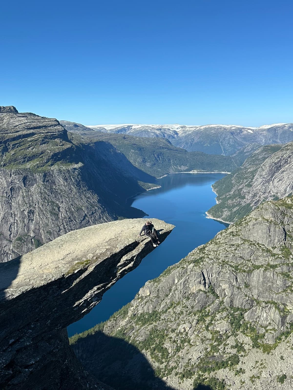 Zwei Personen sitzen auf der Felszunge Trolltunga über einem blauen See