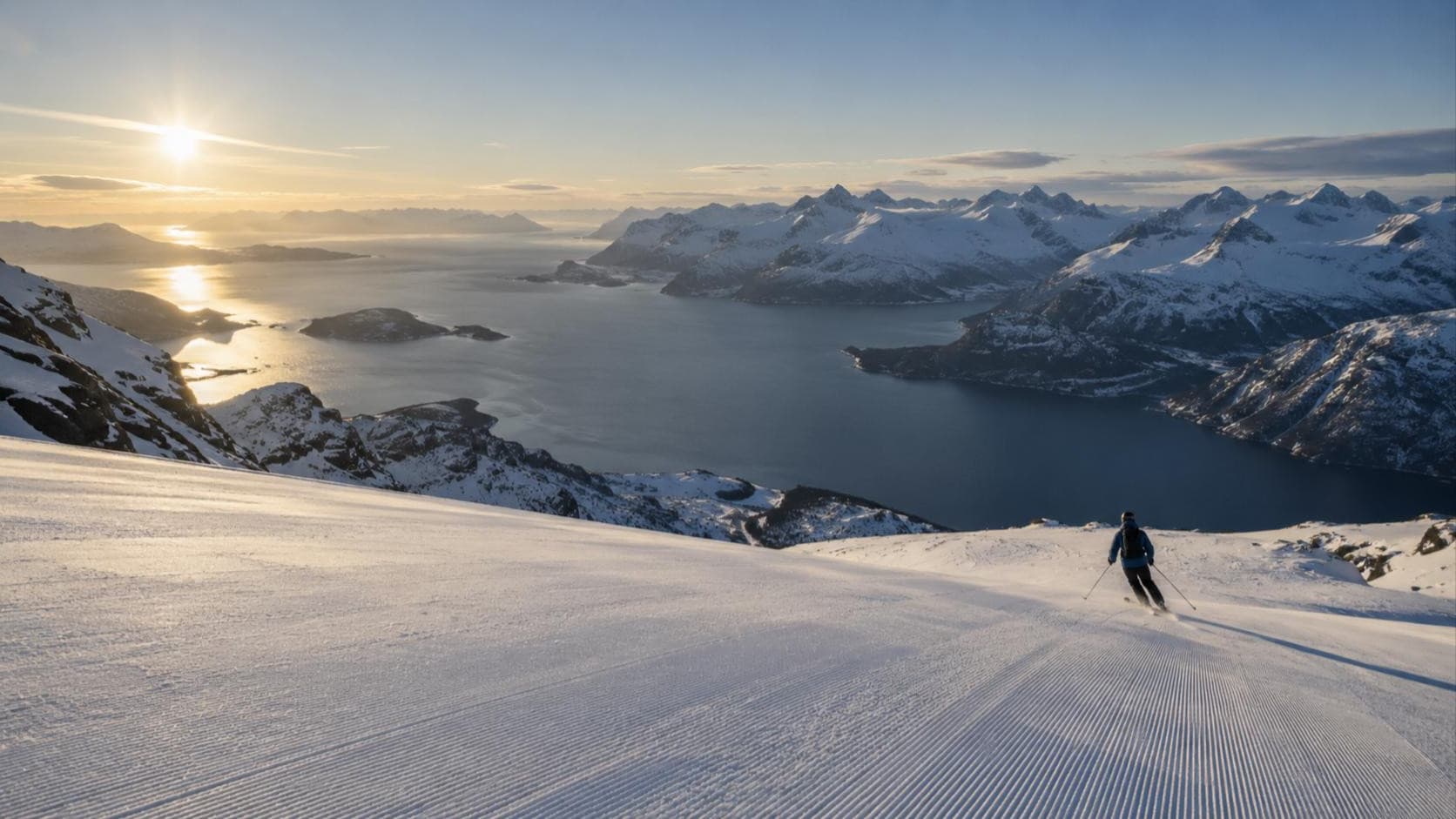 Skifahrer von hinten auf einer präparierten Piste hoch über einem Fjord in der tiefen Wintersonne