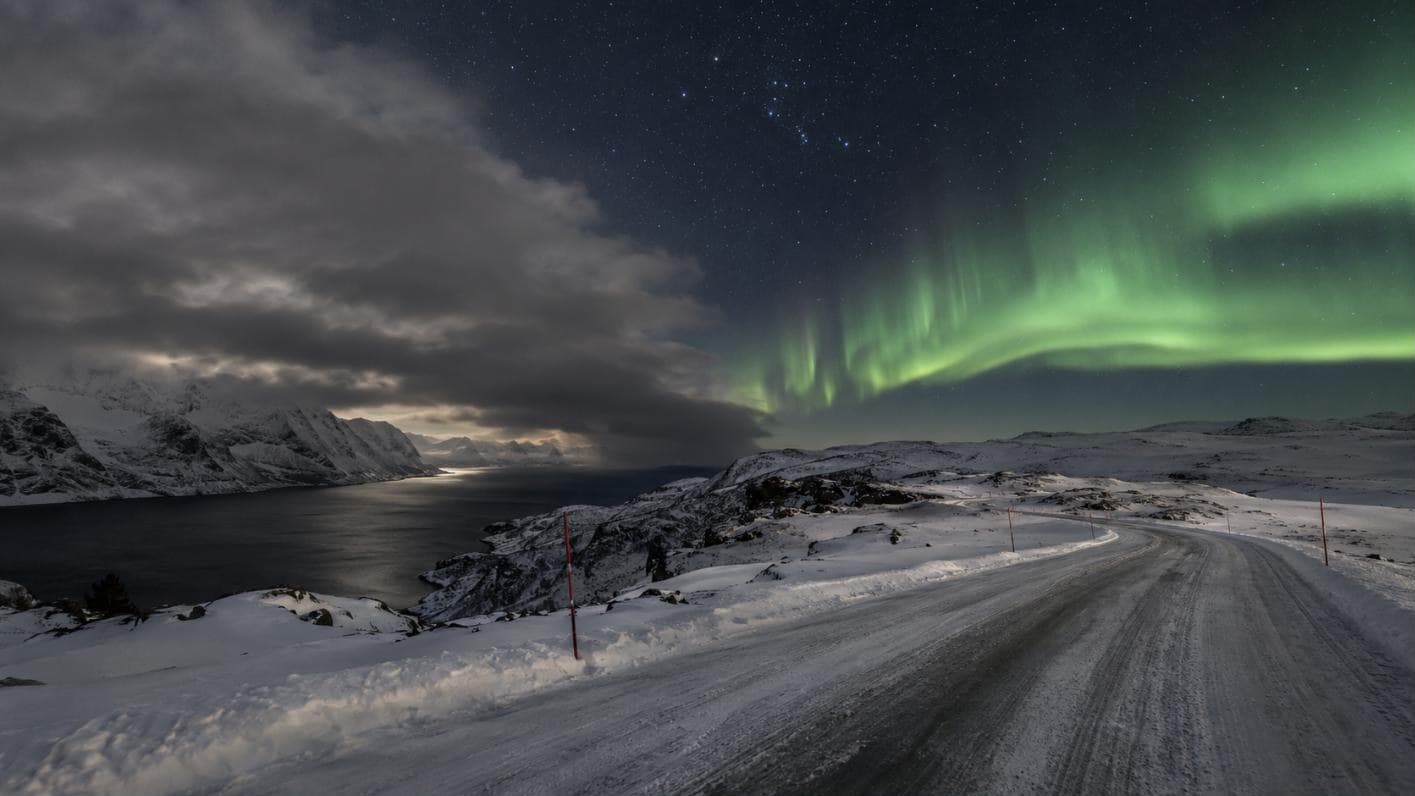 Wolkenbank über dem Küstenfjord links, klarer Himmel mit Nordlicht über dem Inland rechts