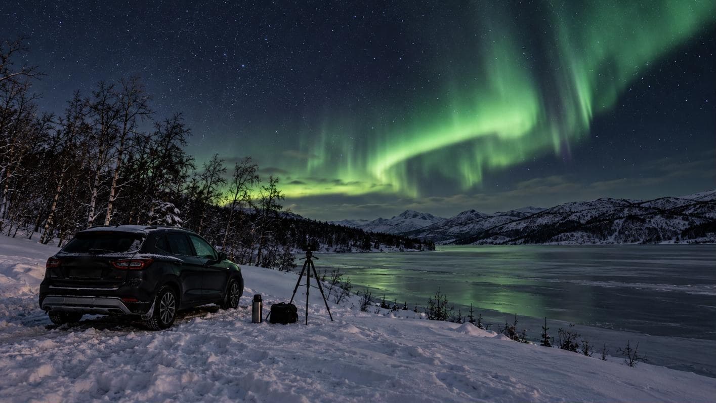 Parkendes Auto mit Stativ am zugefrorenen See im Inland unter hellen Polarlichtern